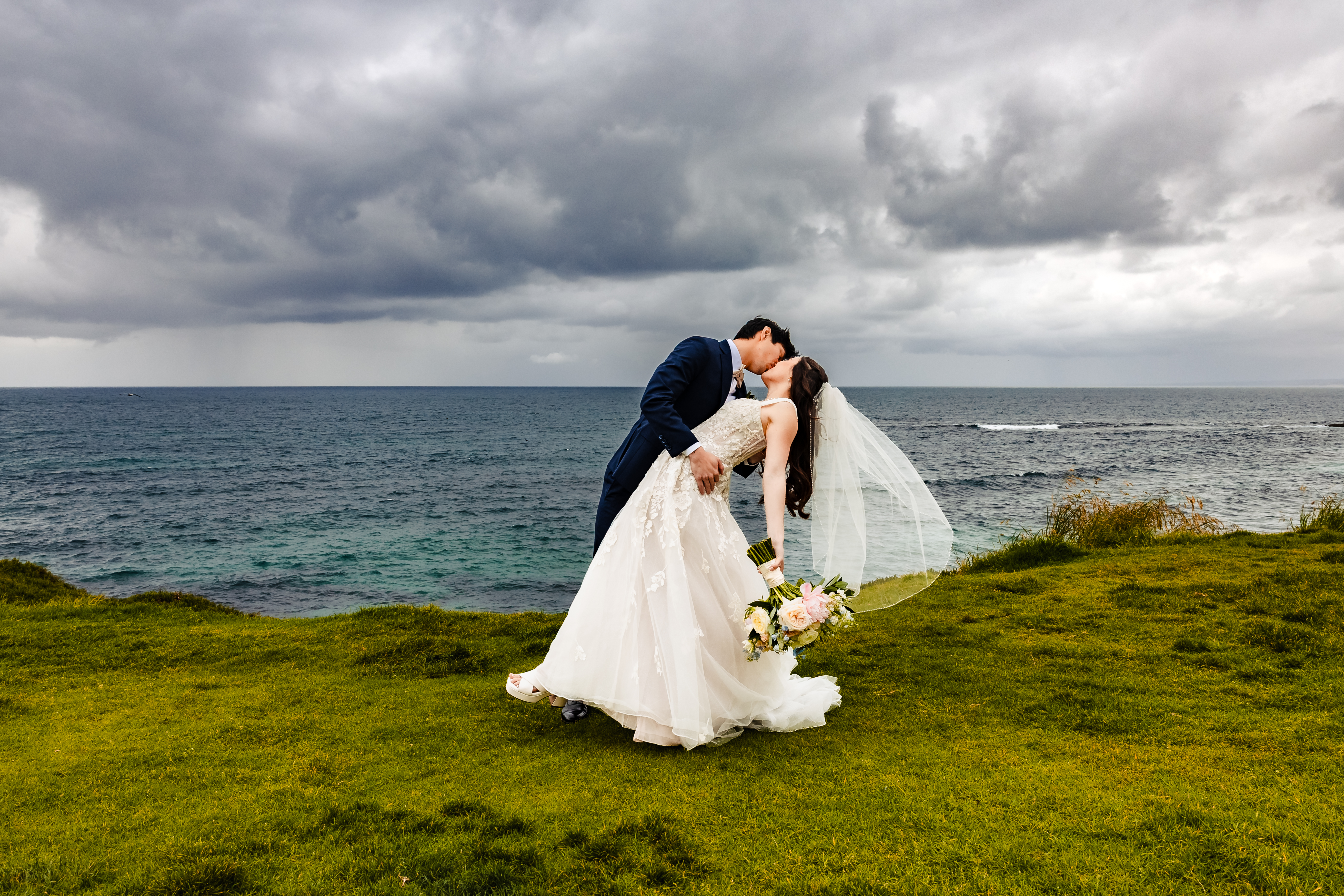 A Catholic couple on the San Diego cliffs with a storm behind them after their nuptial Mass