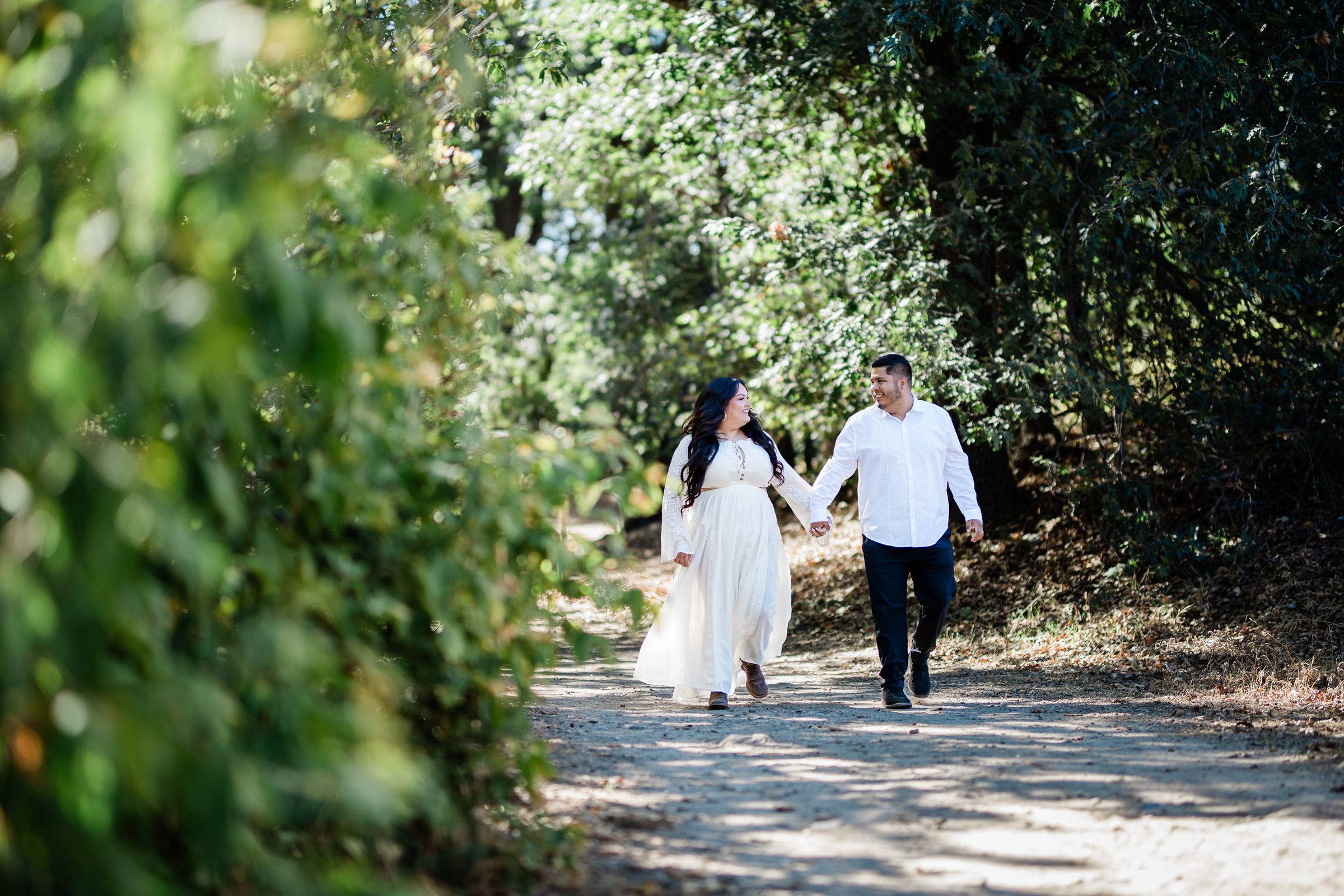 Eric and Cristina walking hand in hand down a shaded trail at Oak Glen Preserve during their engagement session