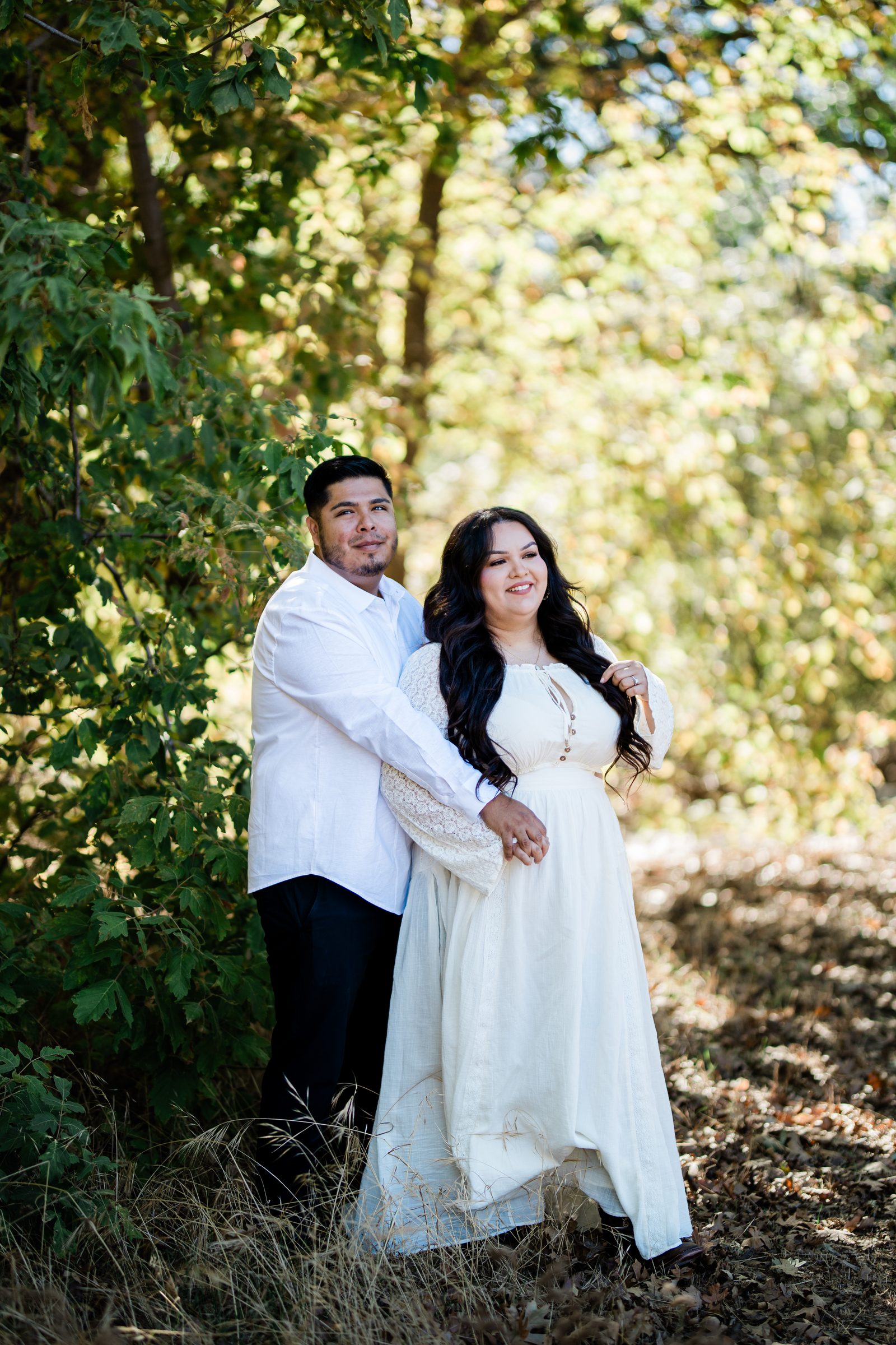 Eric and Cristina embracing among the early-autumn leaves at Oak Glen Preserve