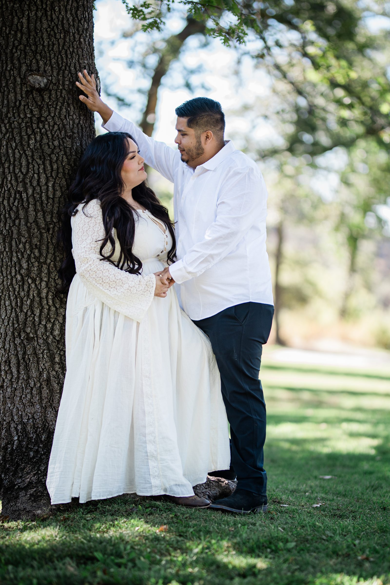 Engaged couple leaning against an oak tree on a green meadow at Oak Glen Preserve