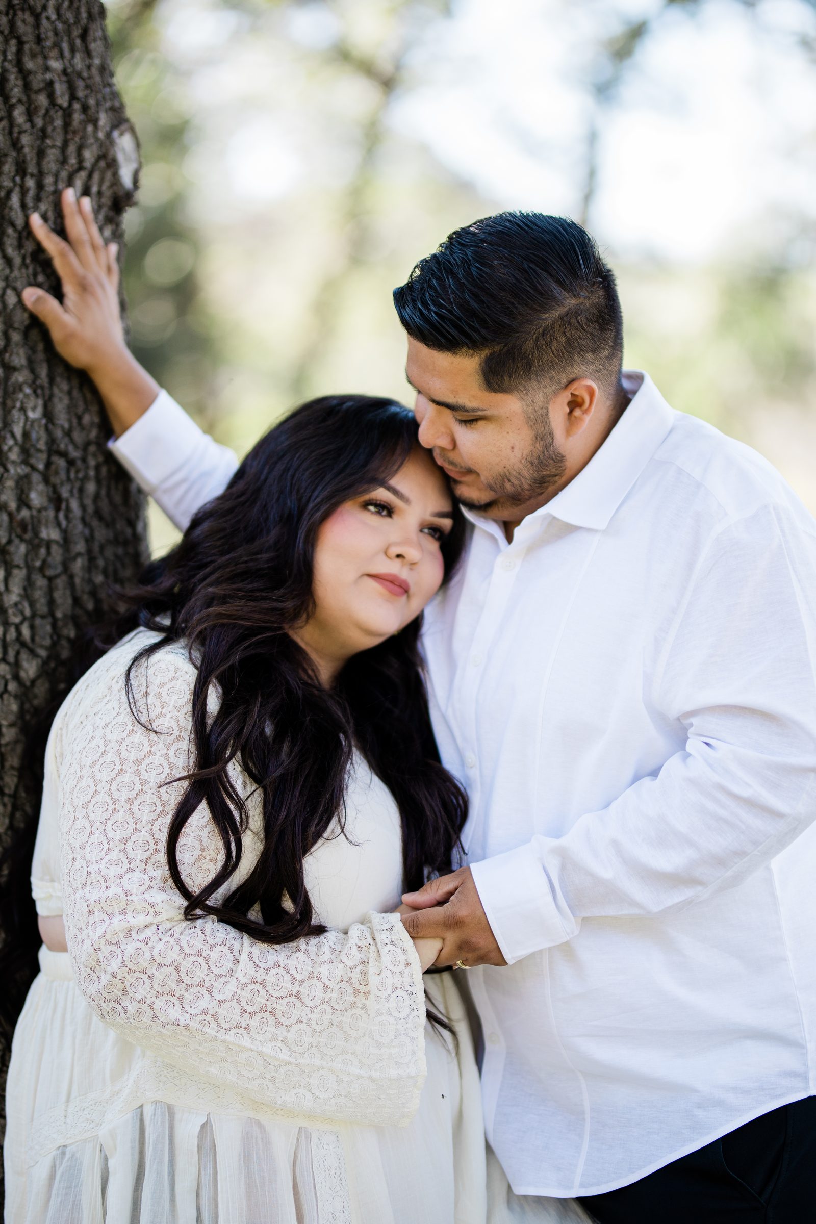 Cristina resting her head on Eric's chest beside an oak at Oak Glen Preserve