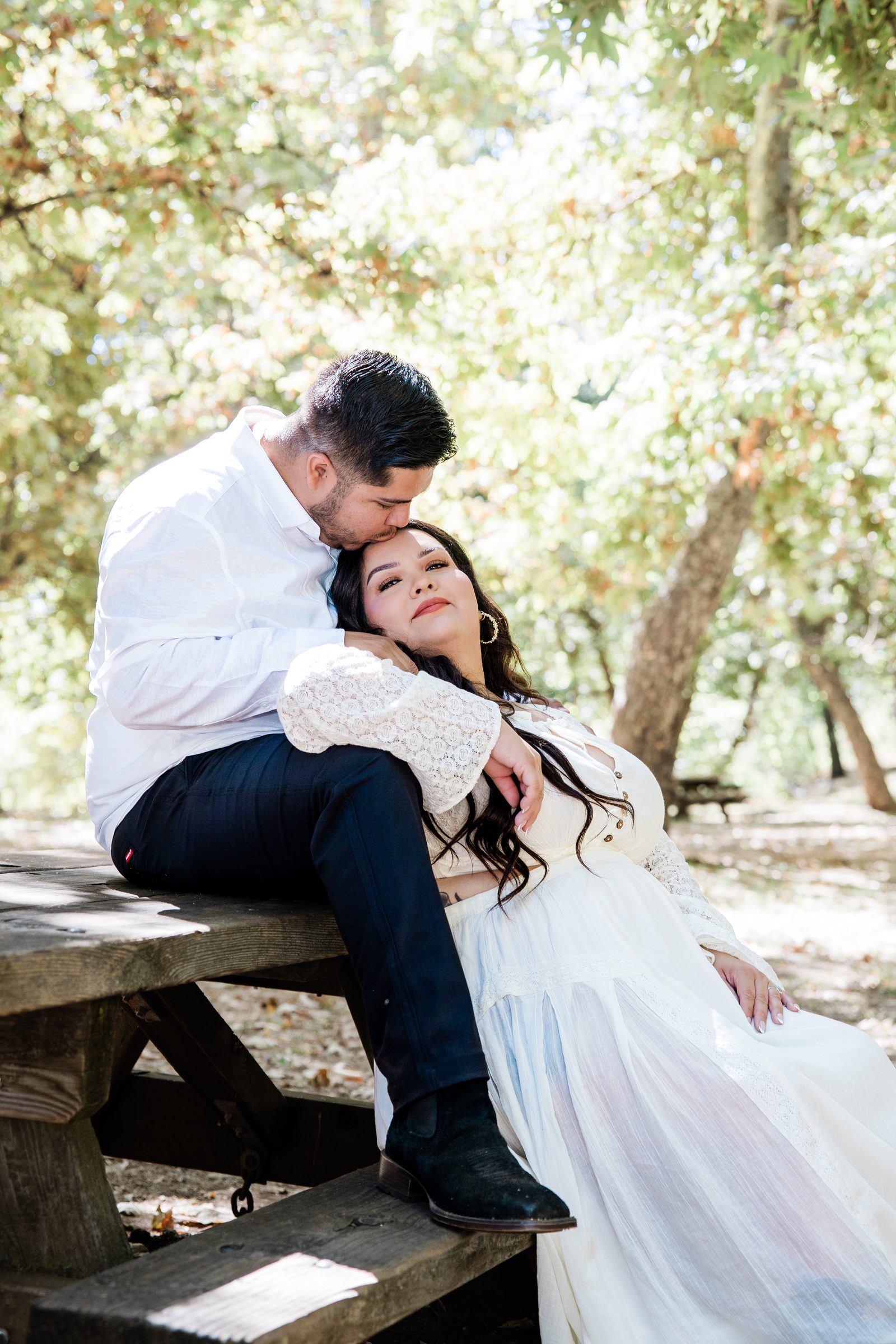 Eric and Cristina resting together on a wooden picnic table under the trees at Oak Glen Preserve