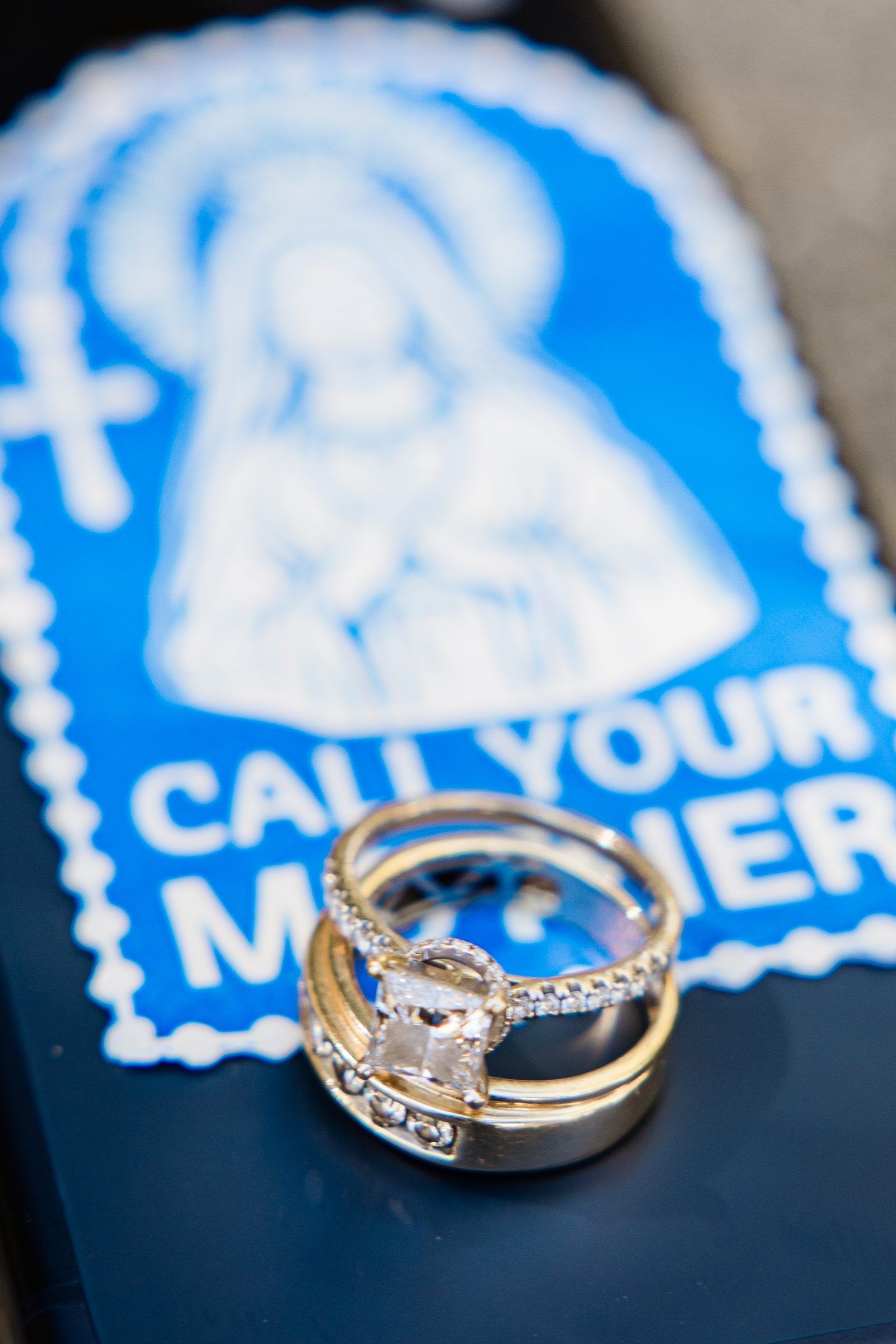 Engagement ring and wedding bands resting on an image of Our Lady reading Call Your Mother