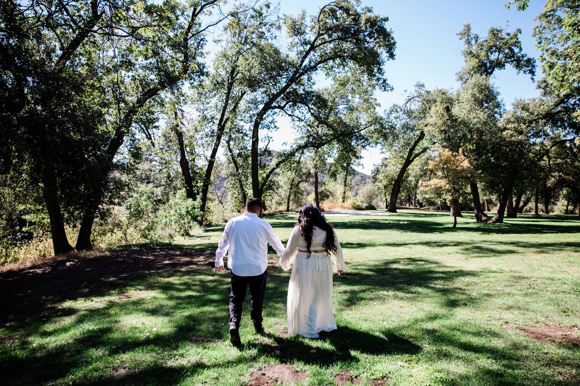 Eric and Cristina walking together across a broad lawn beneath tall oaks at Oak Glen Preserve