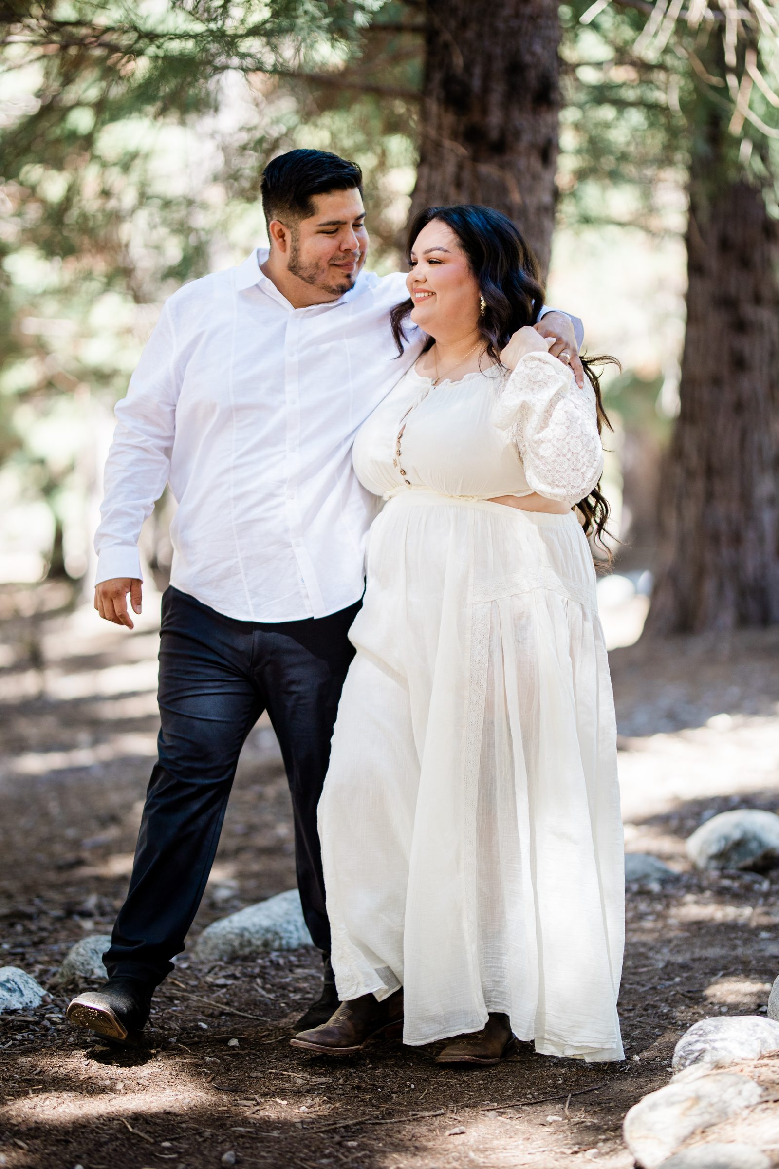 Eric and Cristina smiling together among the pines at Oak Glen Preserve