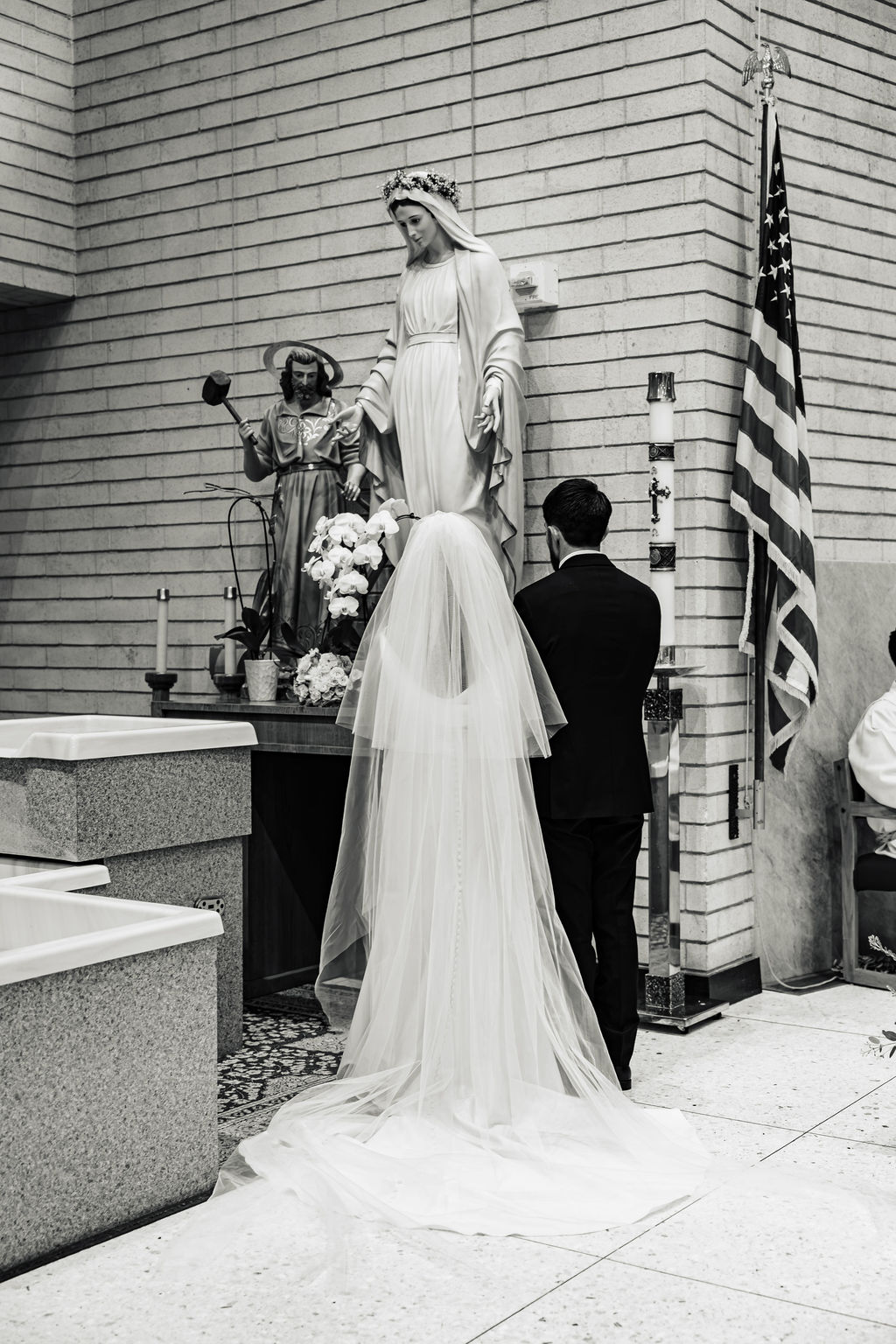 PJ and Sarah at the statue of the Virgin Mary, a black and white photograph from their wedding at Saint Mary's Catholic Church