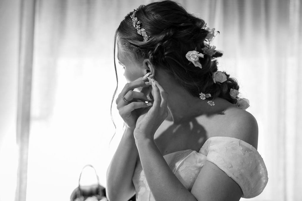 Black and white of the bride putting in her earrings