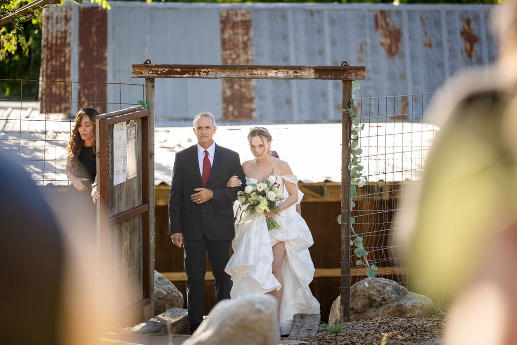 The bride and her father through the rustic wooden gate