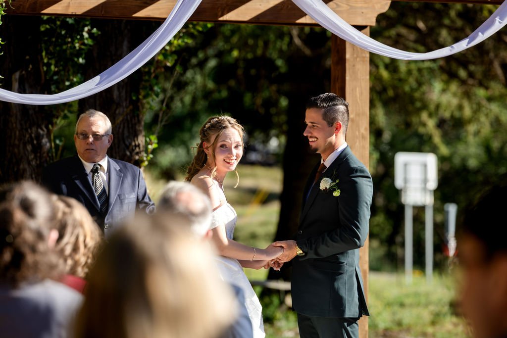The couple holding hands beneath the white-draped arbor