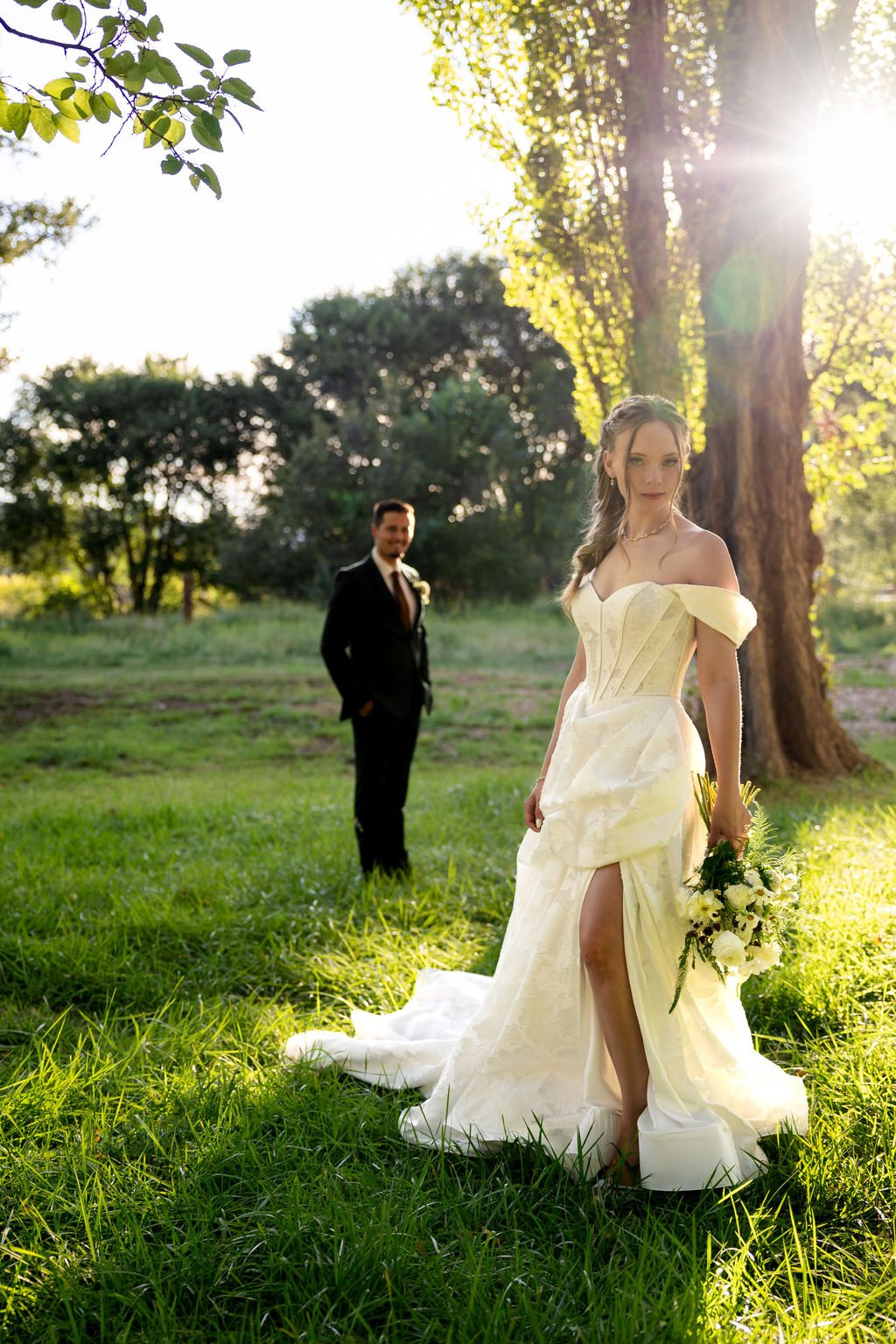 The bride in the sunlit meadow with the groom behind her