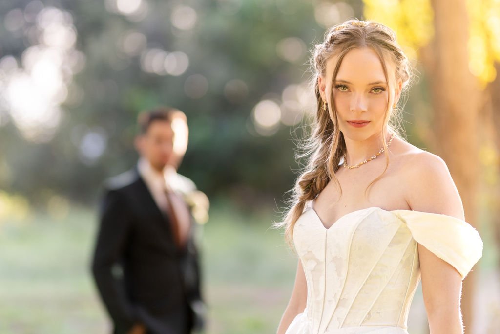 The bride looking into the camera with the groom softly behind her
