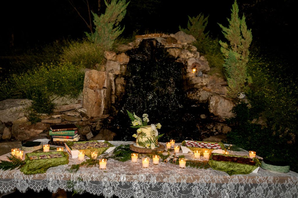The candlelit dessert table beside the rock falls at night