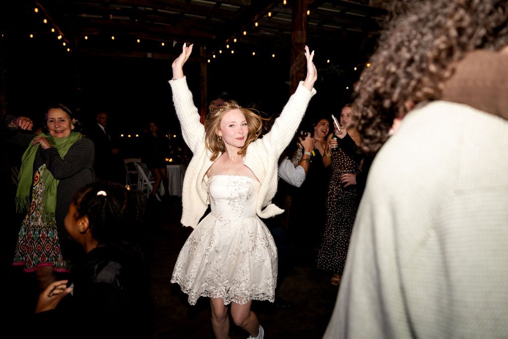 The bride in her short reception dress dancing with her arms raised
