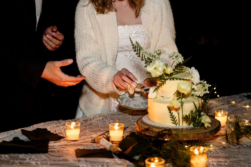 Francis and Aubrey cutting their wildflower wedding cake by candlelight