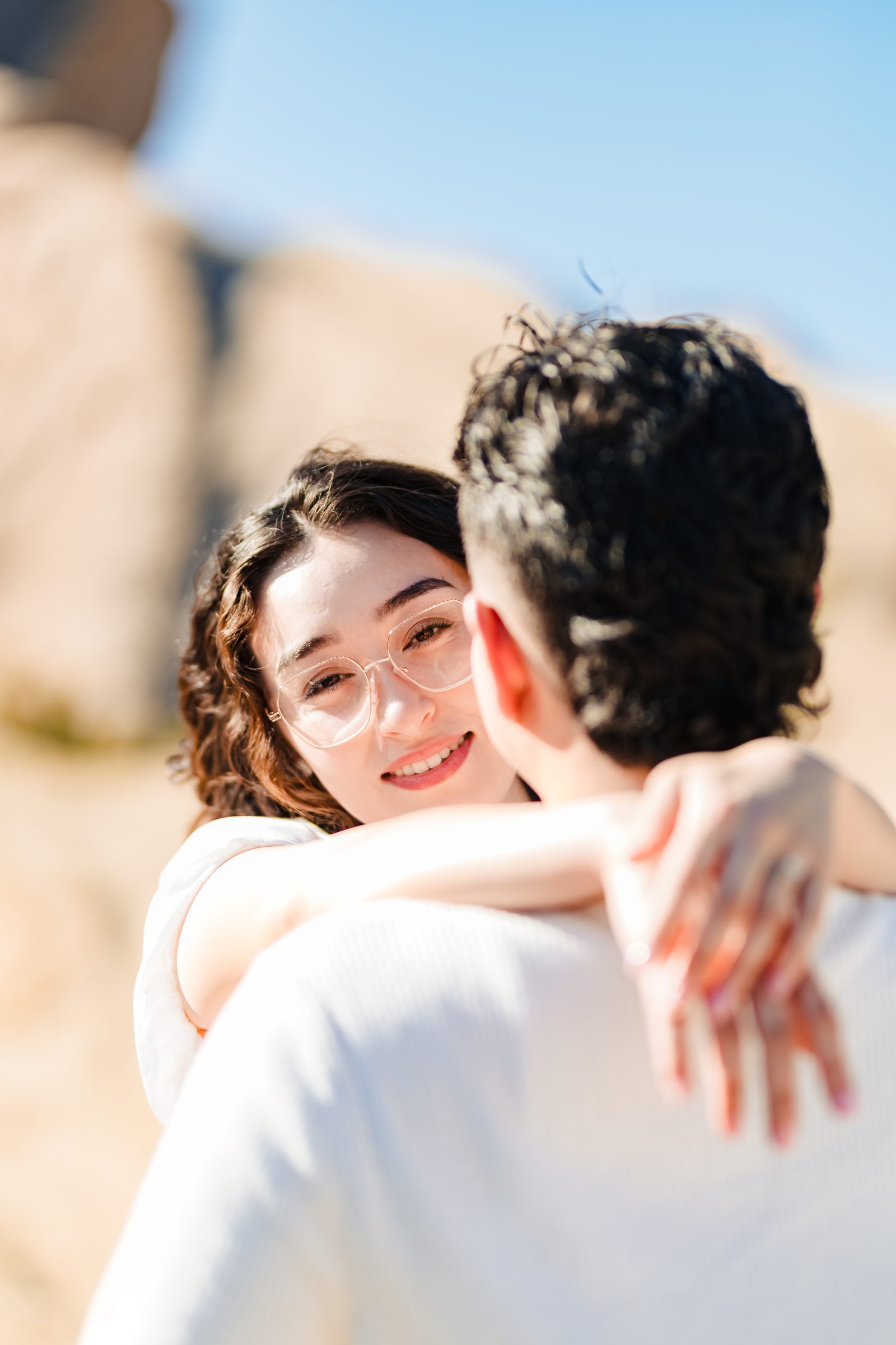 Daniela smiling over Enrique's shoulder in the desert sun