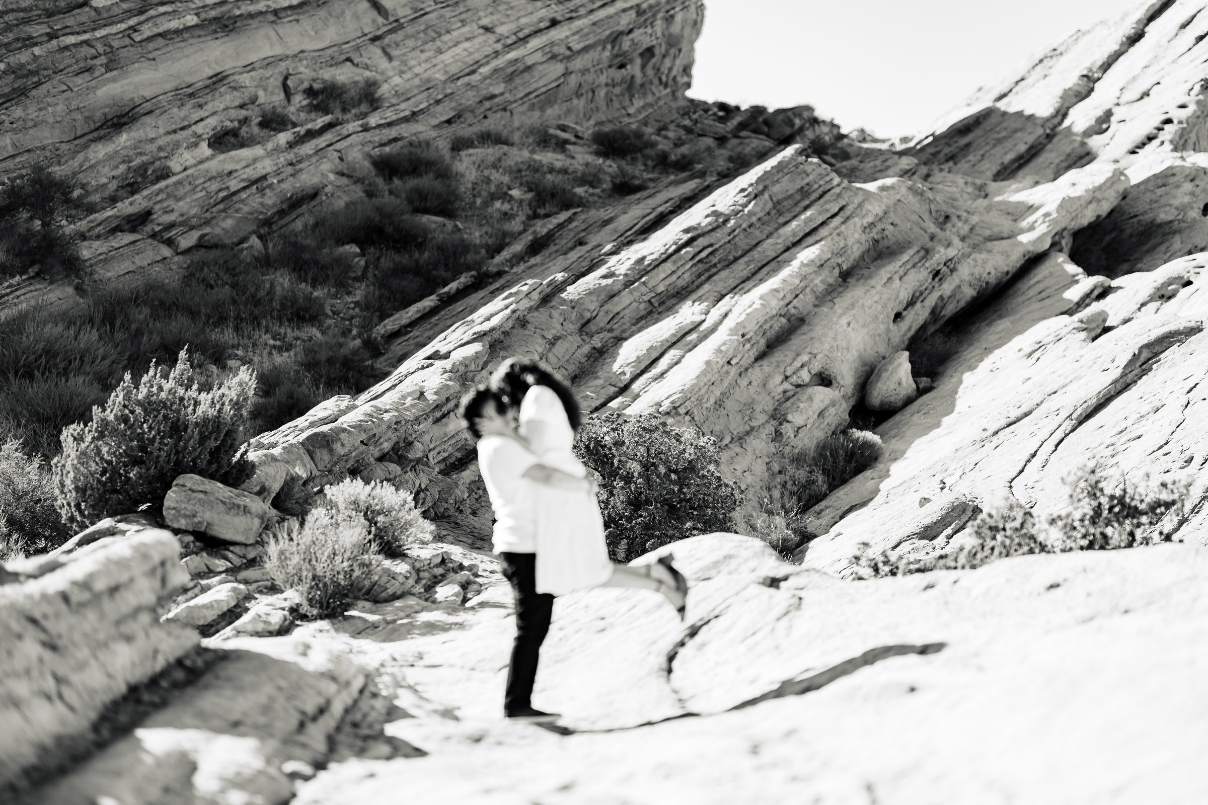 Black and white of the couple kissing beneath the tilted rock formations