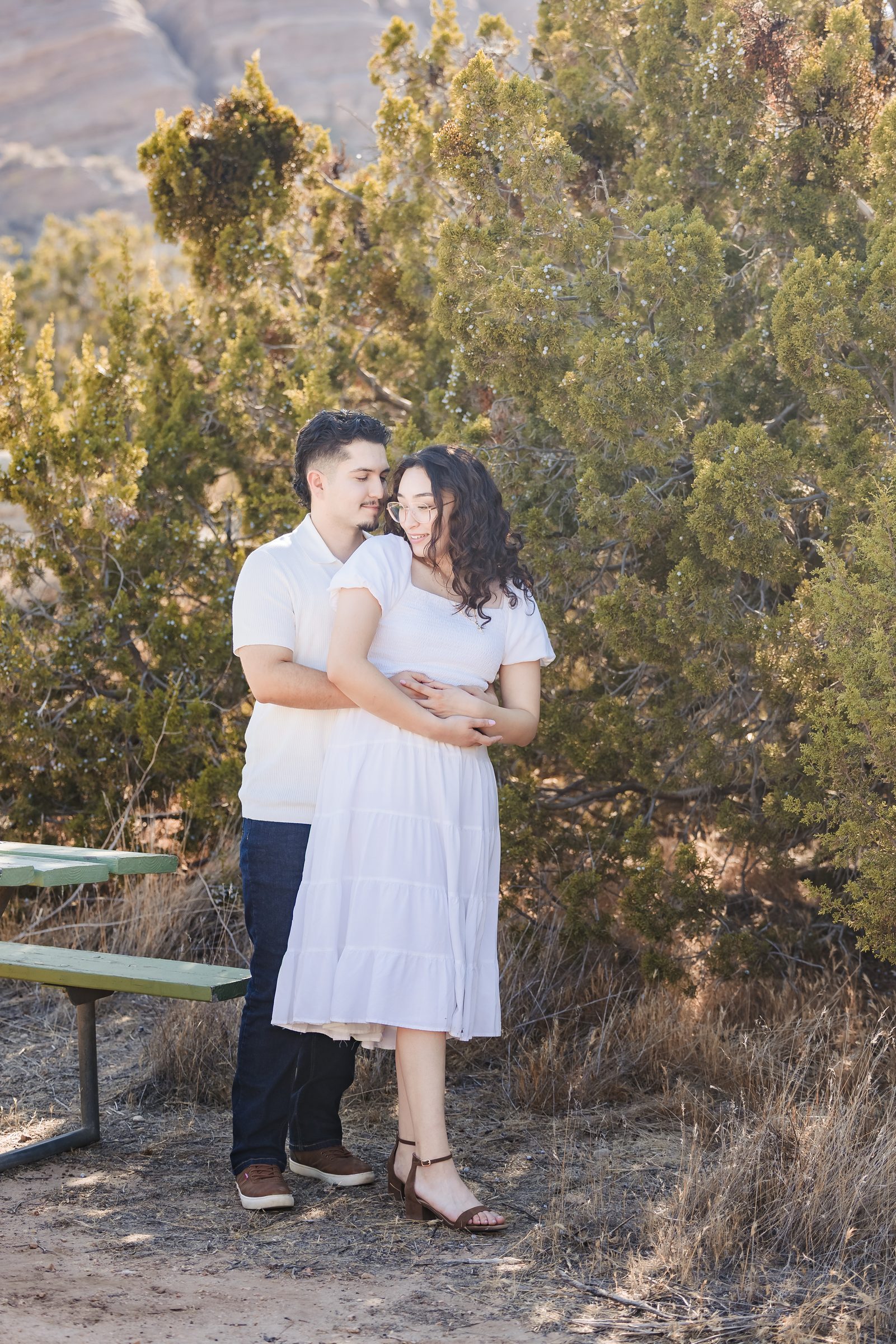 Enrique holding Daniela from behind beside the desert trees