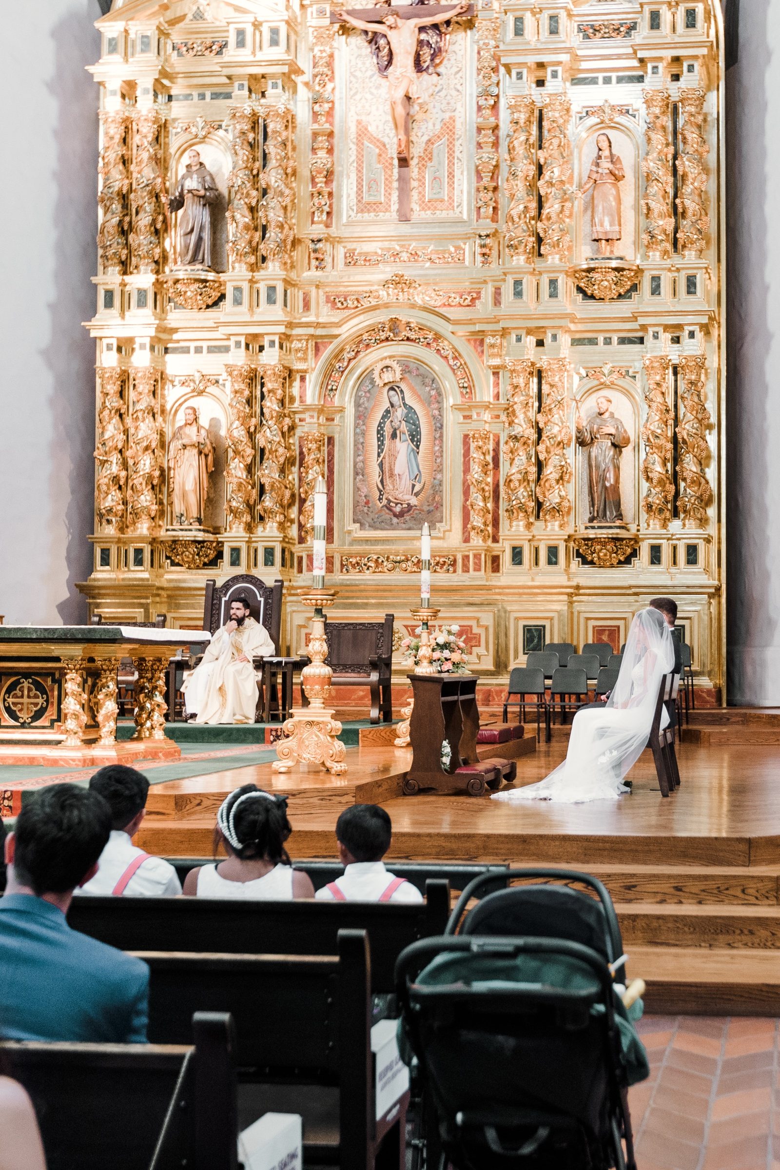 A couple seated before the gilded retablo of Mission Basilica San Juan Capistrano