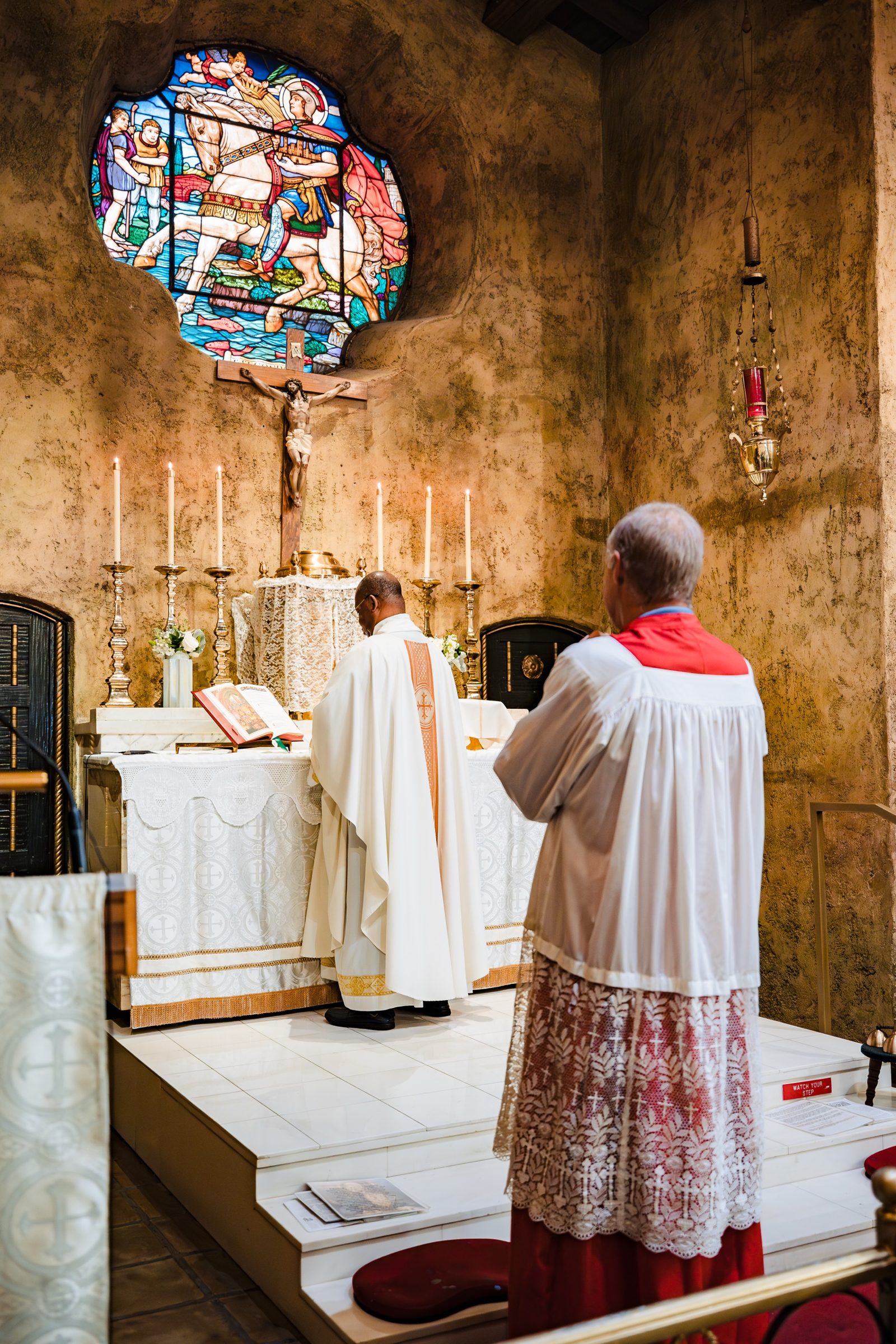 The priest at the altar beneath the round stained glass window of St. Secundus at San Secondo d'Asti