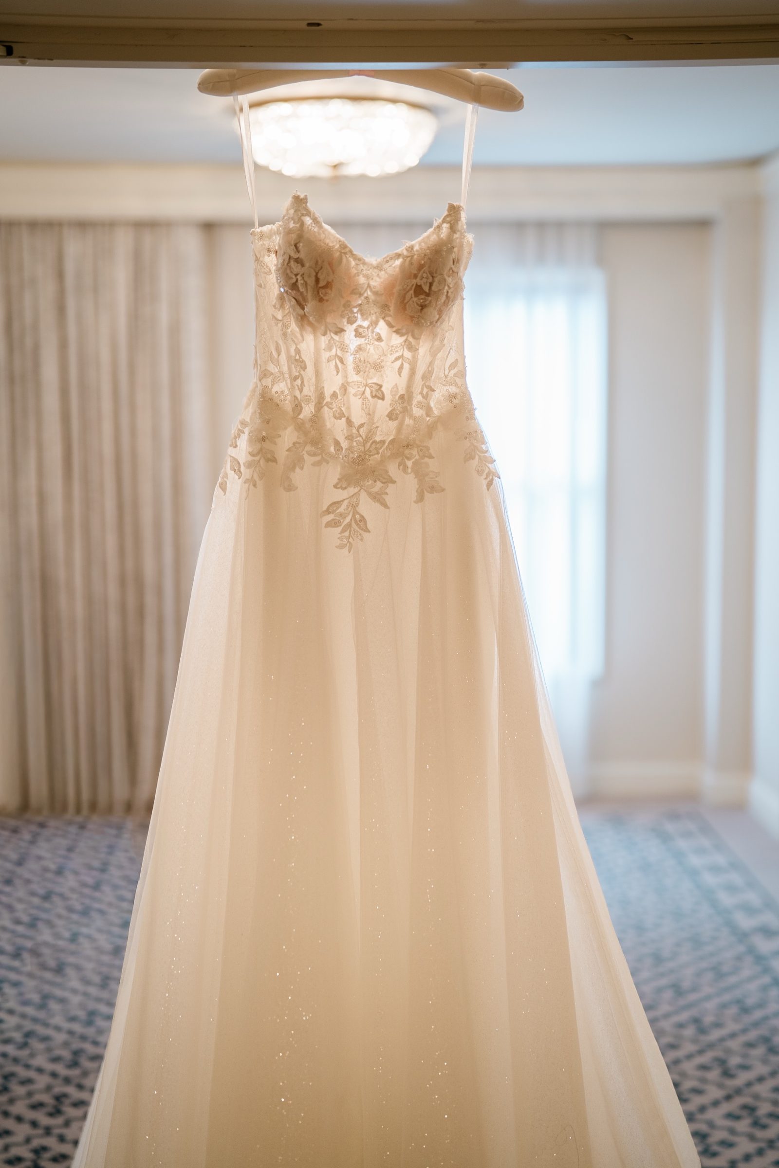The wedding gown hanging in the window light