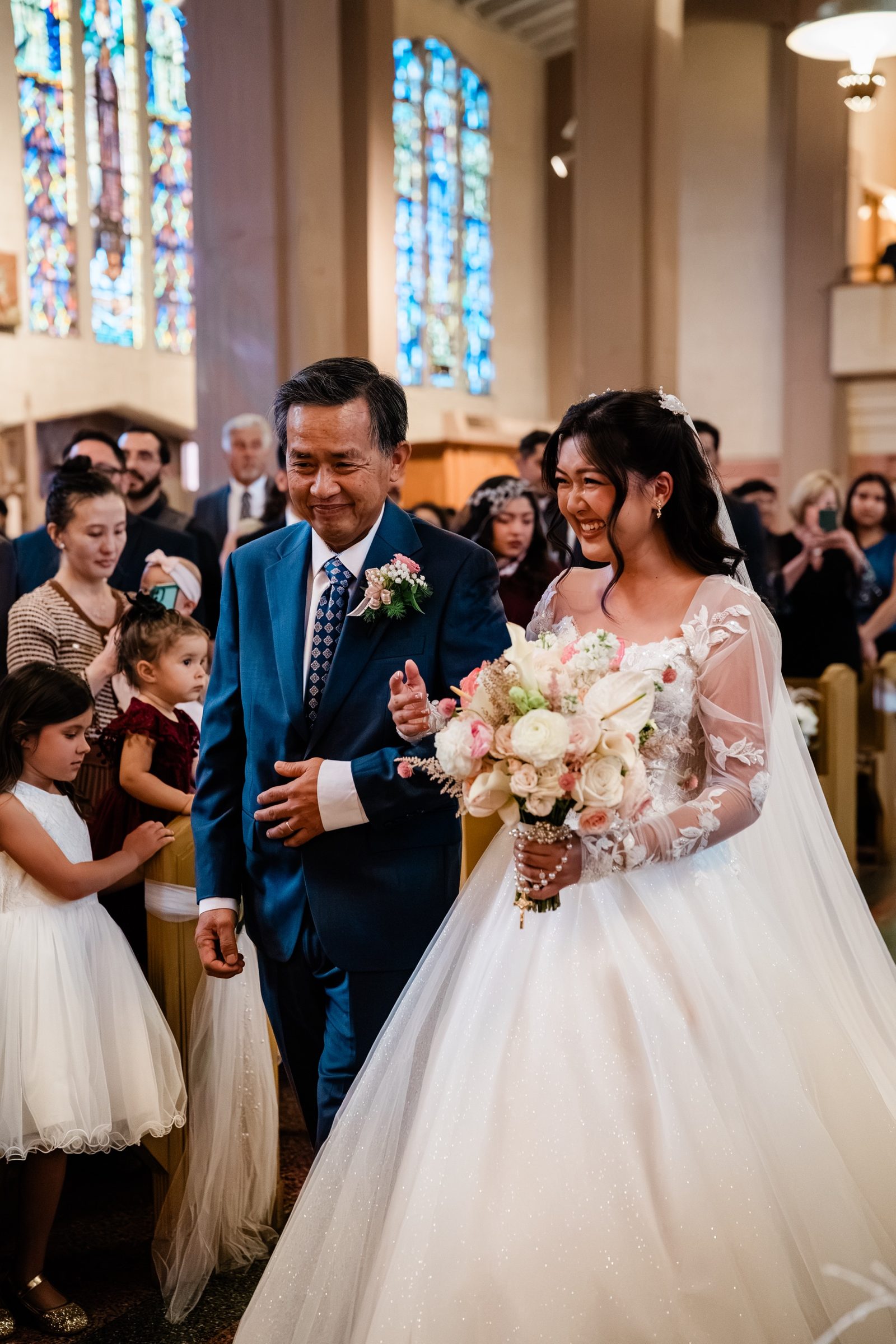 Candice and her father smiling on the aisle as the flower girls look on