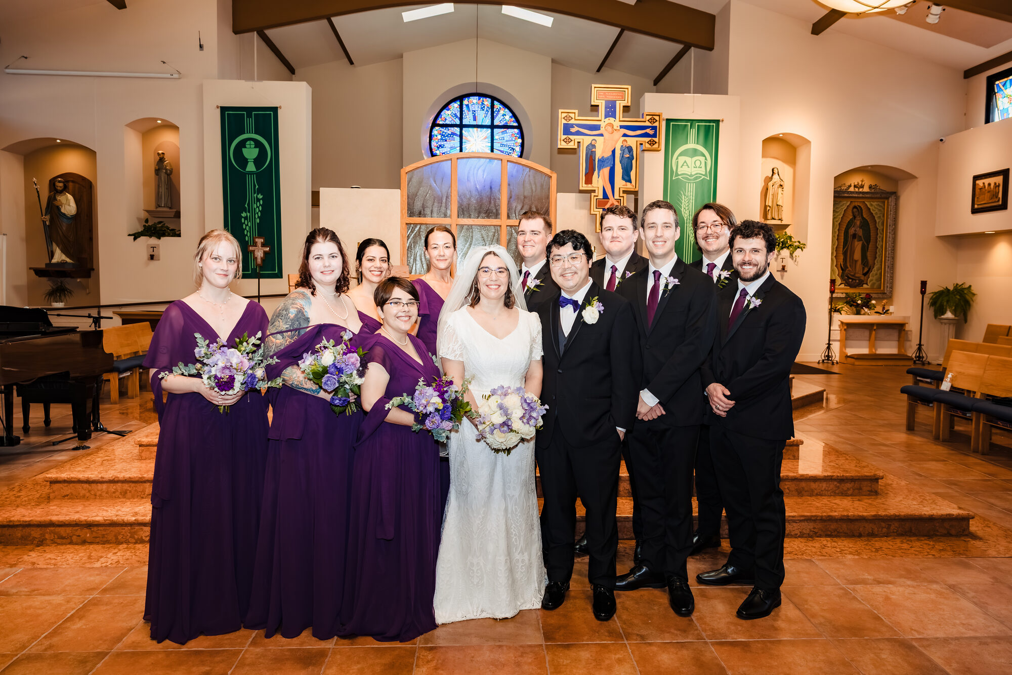 Wedding party portrait at Our Lady of Guadalupe, bridesmaids in deep purple and groomsmen in black suits with burgundy ties