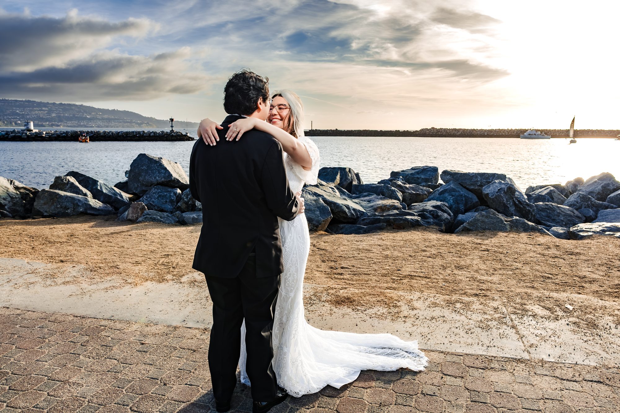 Bride wrapping her arms around the groom at golden hour by the harbor