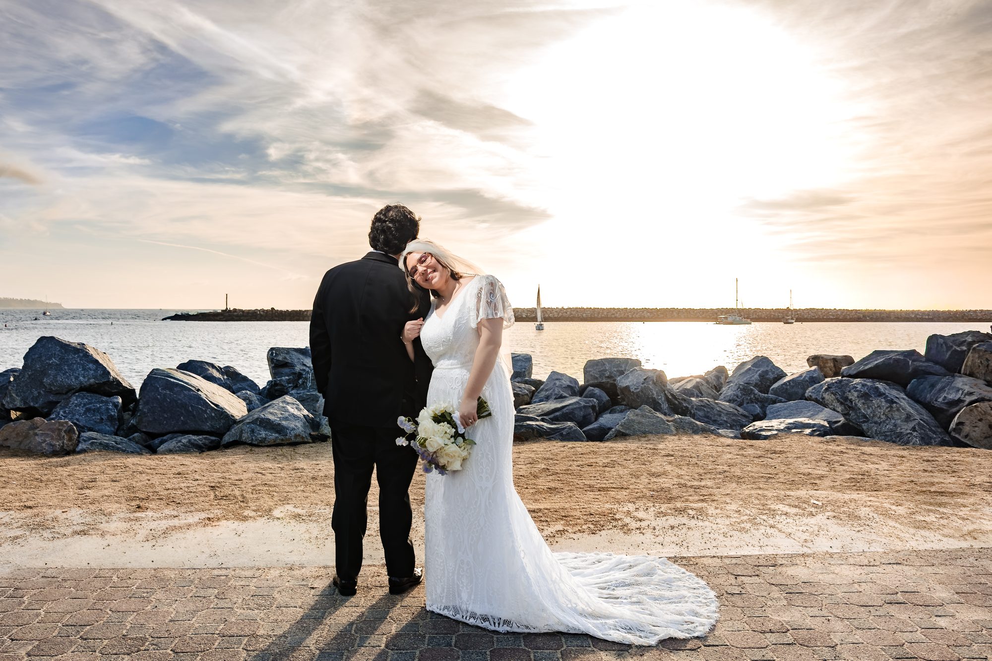 Bride laughing with her white and lavender bouquet beside the groom at sunset