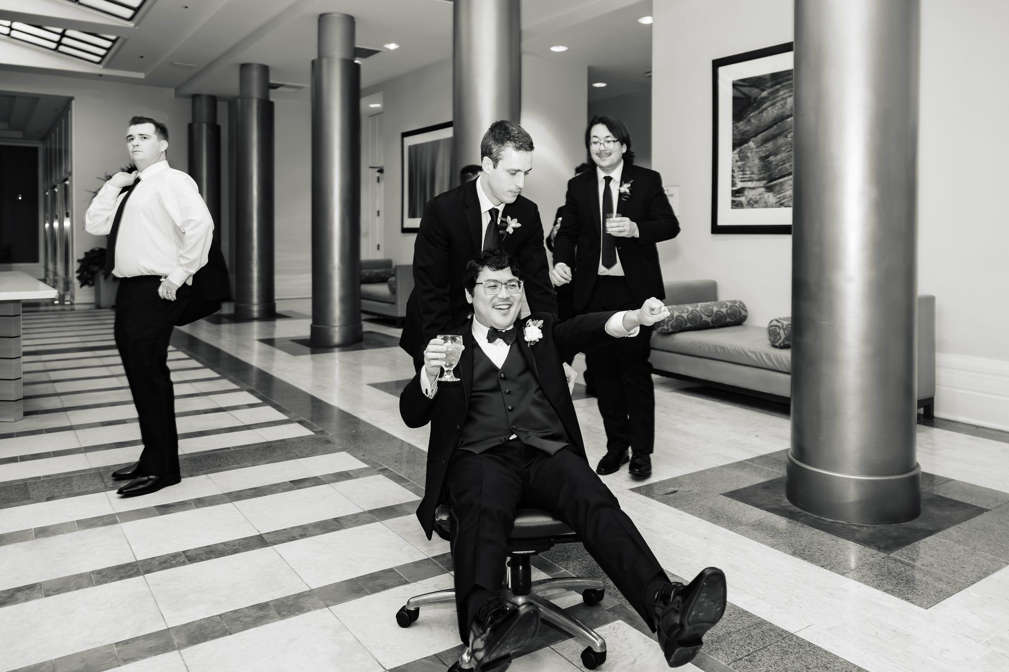 Black and white candid of the groom and his groomsmen celebrating in the lobby