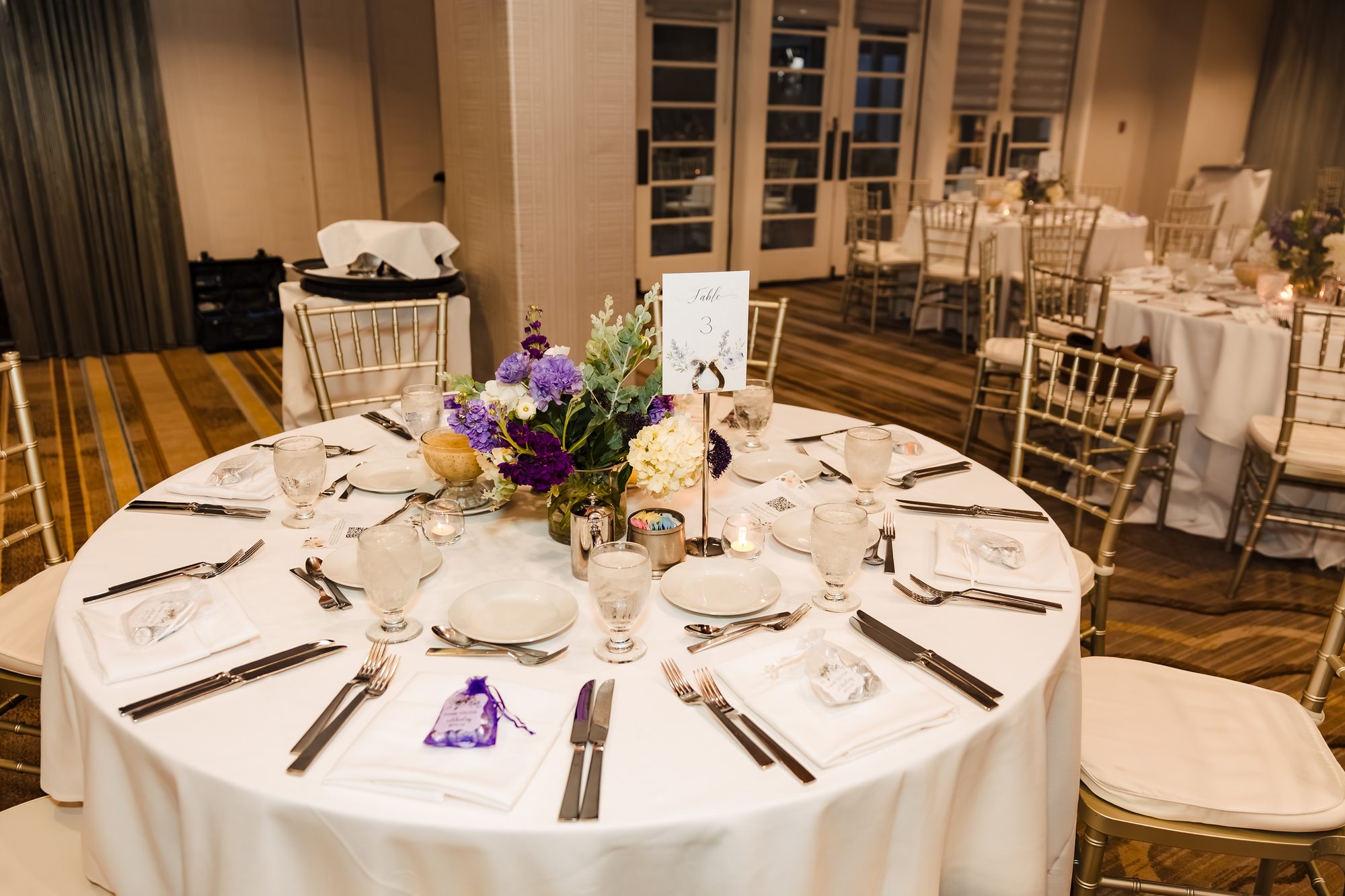 Reception tablescape with purple and white florals and gold chiavari chairs at the Sonesta ballroom