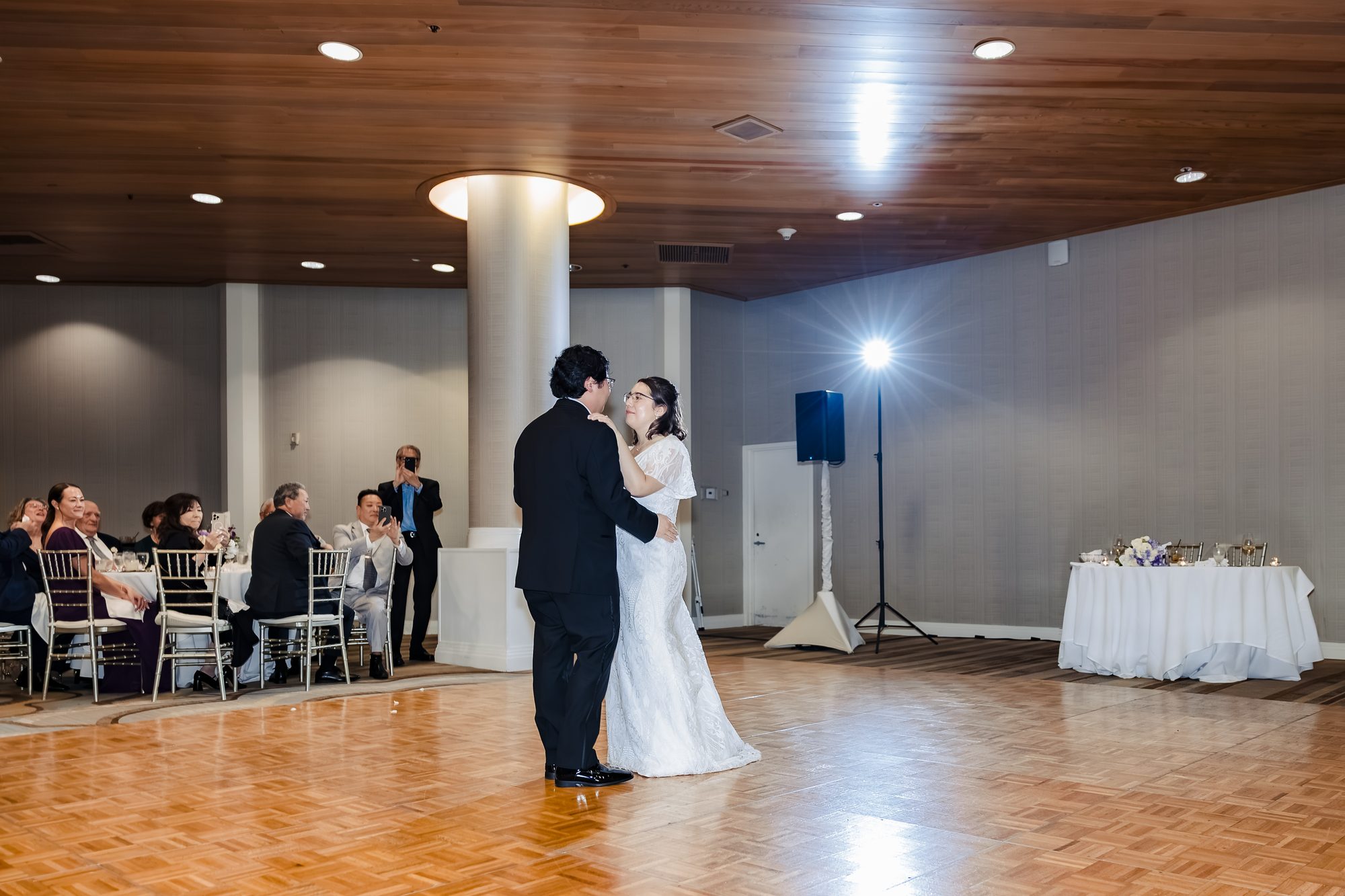 Bride and groom first dance on the parquet floor as guests look on