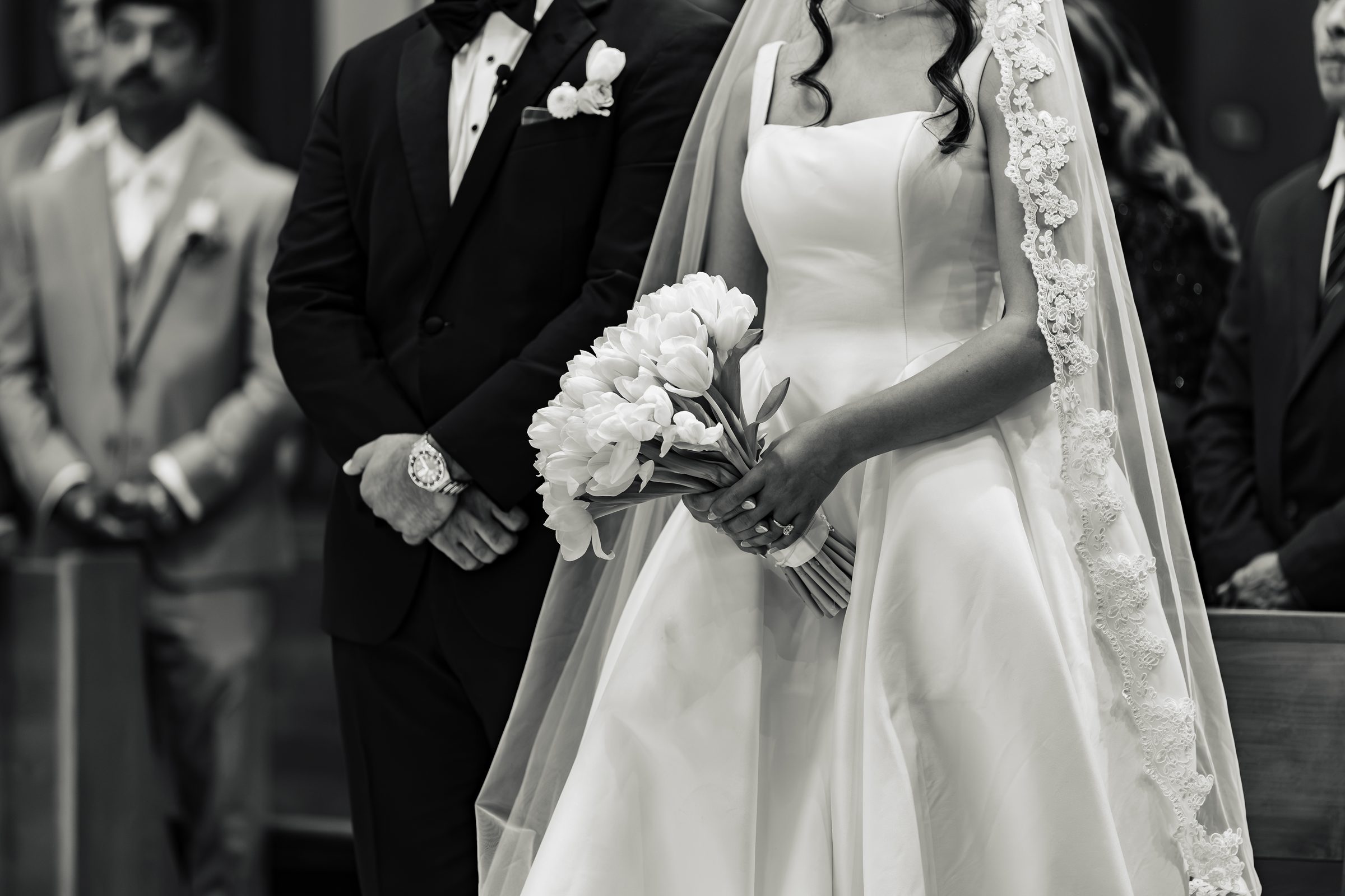 Black and white detail of the bride's bouquet and veil beside the groom