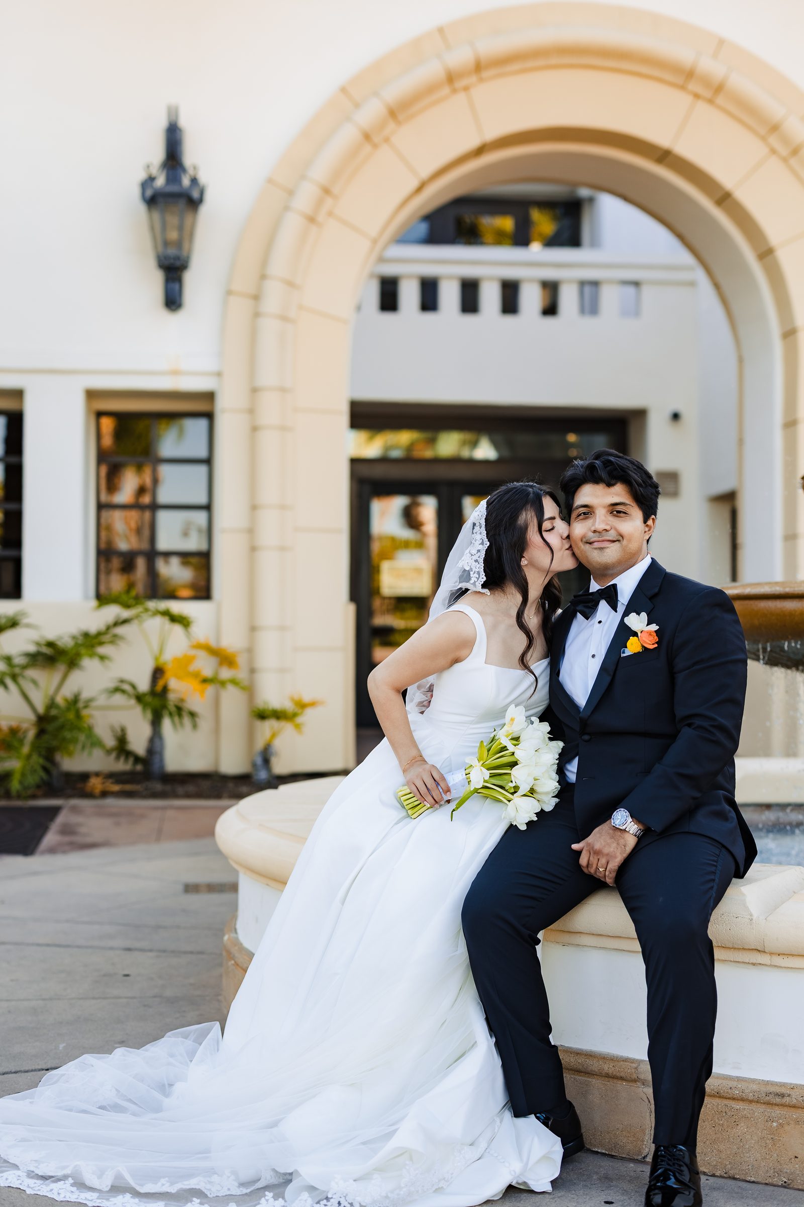 The couple seated on the fountain edge beneath a Spanish arch
