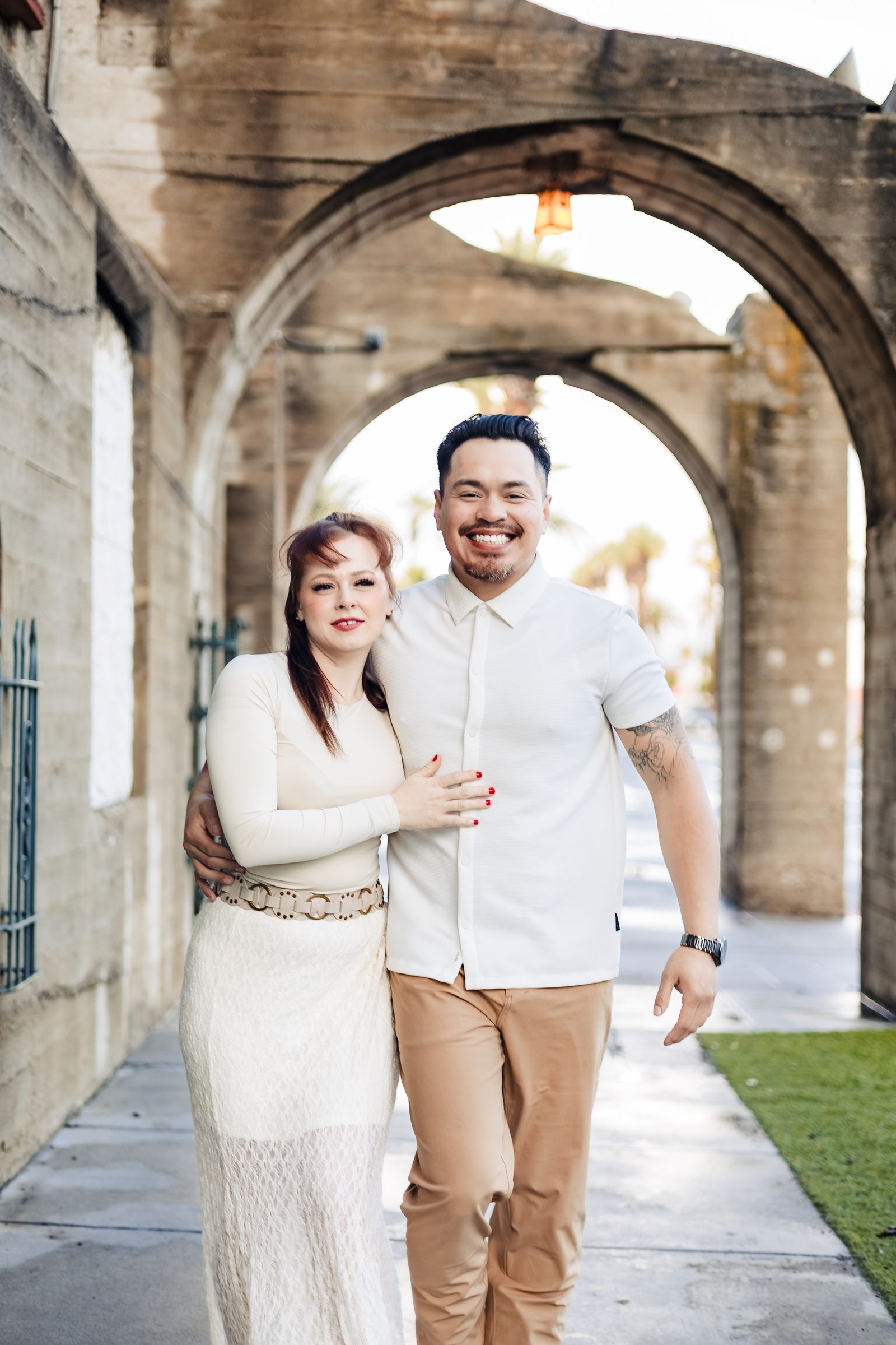 Isaac and Brittany laughing beneath stone arches at the Mission Inn