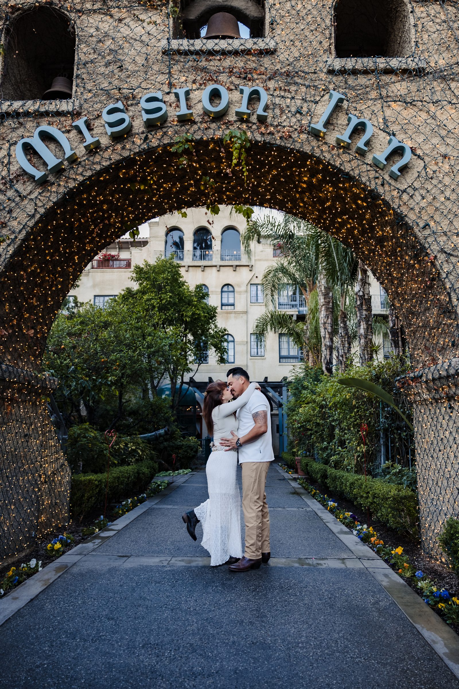 The couple framed by the Mission Inn sign and garden archway
