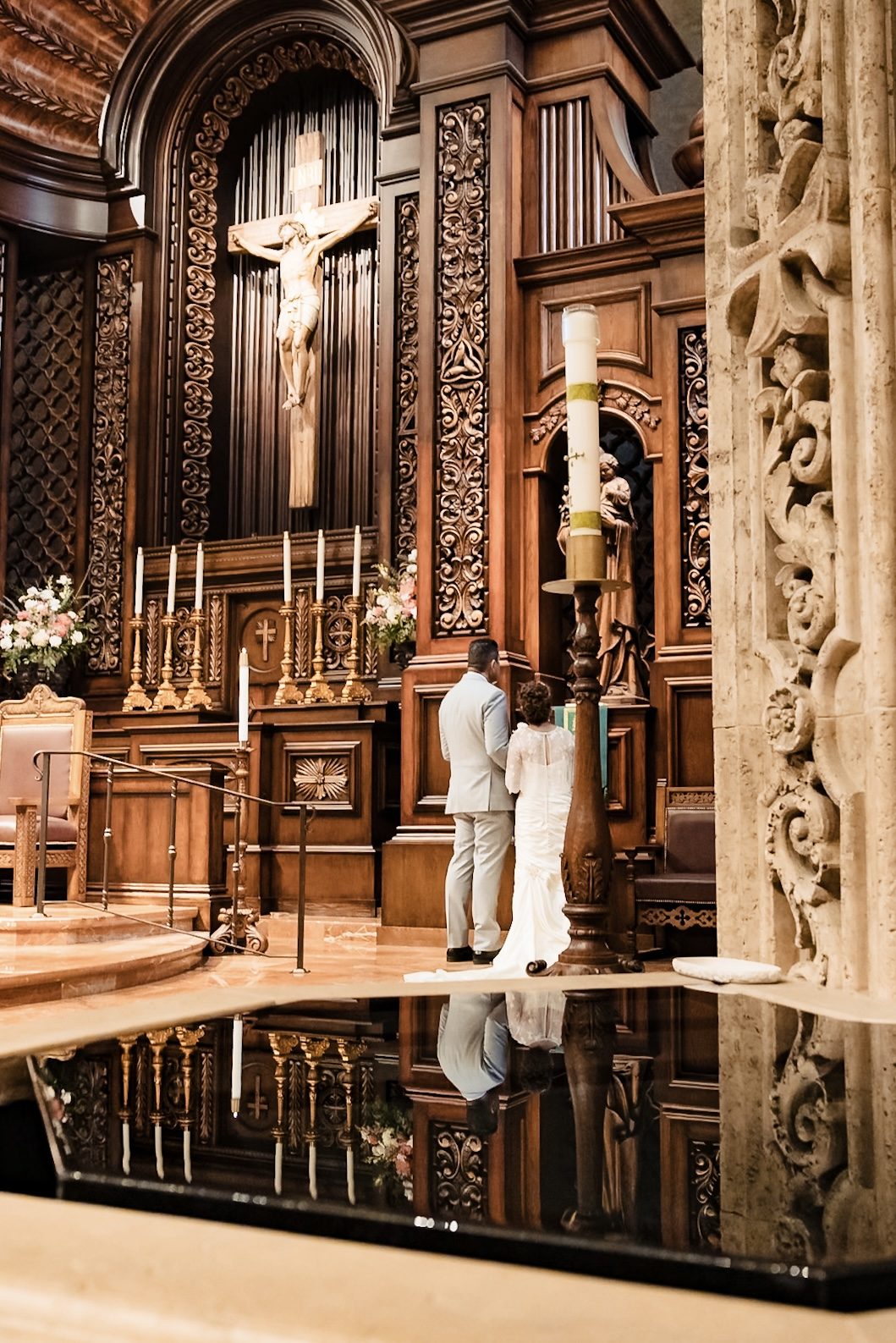 The couple at the side altar reflected in the baptismal font