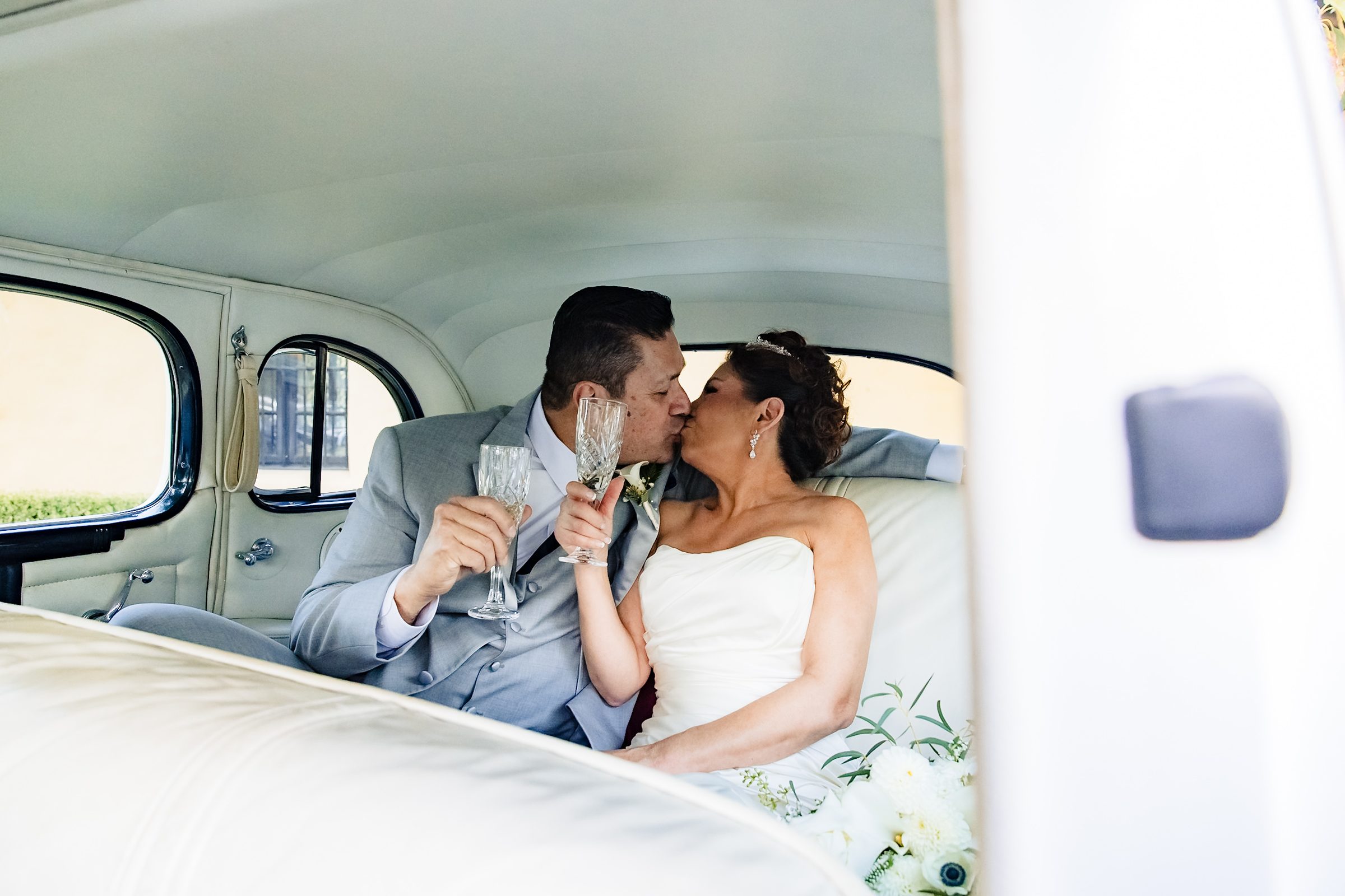 Joe and Victoria toasting with crystal glasses in the back of the classic car